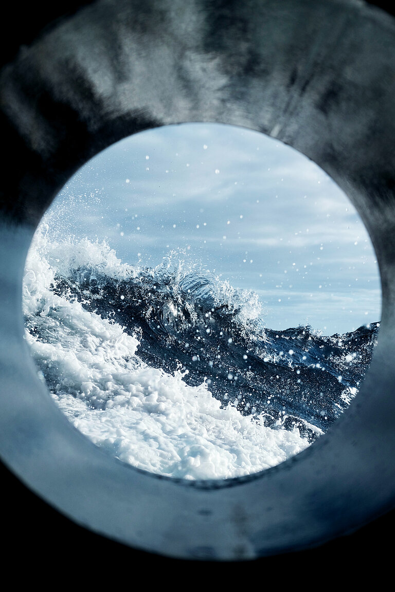 You can see waves, spray and the sky through the scuppers of a ship.
