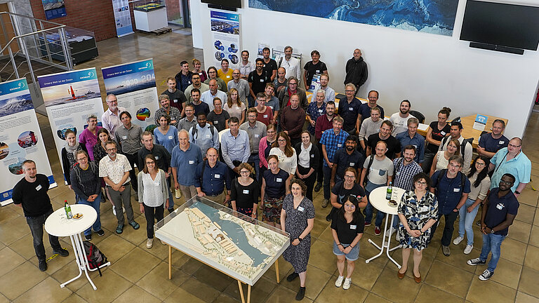 Eine Gruppe Menschen steht in einem Foyer. Alle schauen in die Kamera.