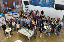 A group of people are standing in a foyer. They are all looking at the camera.