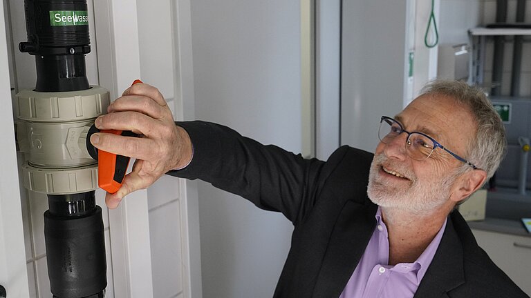 Ein Mann in lila Hemd und Anzugjacke dreht einen großen roten Hahn auf