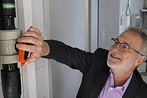 A man in a purple shirt and suit jacket turns on a large red tap