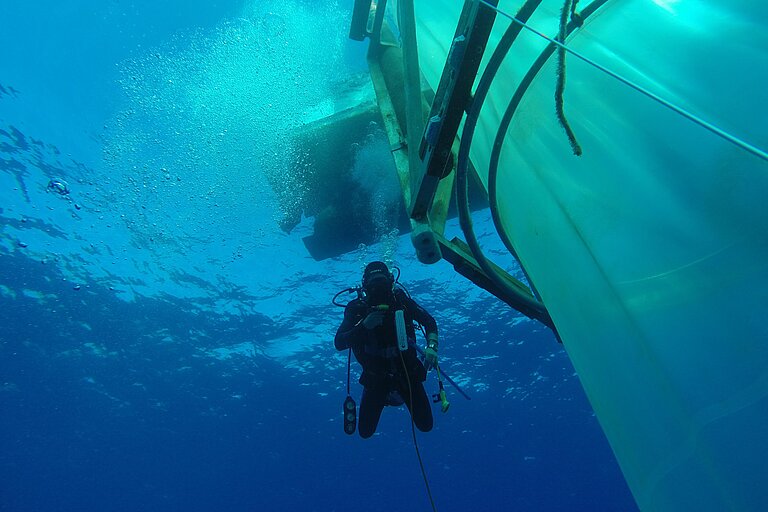 Next to a mescocosmo a diver sinks in clear blue water into the depths. Photo: Michael Sswat/GEOMAR