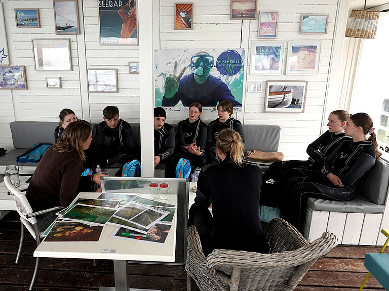 Jugendliche in Neoprenanzügen beim Theorie-Unterricht vor dem Schnorcheln.