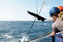 Zwei Mitarbeiter auf einem Forschungsschiff lassen ein Messgerät zu Wasser