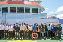 Schiffscrew in weißen Hemden und schwarzen Hosen und wissenschaftliche Crew und Besucher posieren auf dem Helikopterdeck eines Forschungsschiffes