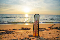 Ein Thermometer steckt am Strand im Sand und zeigt 40 Grad Celsius an.