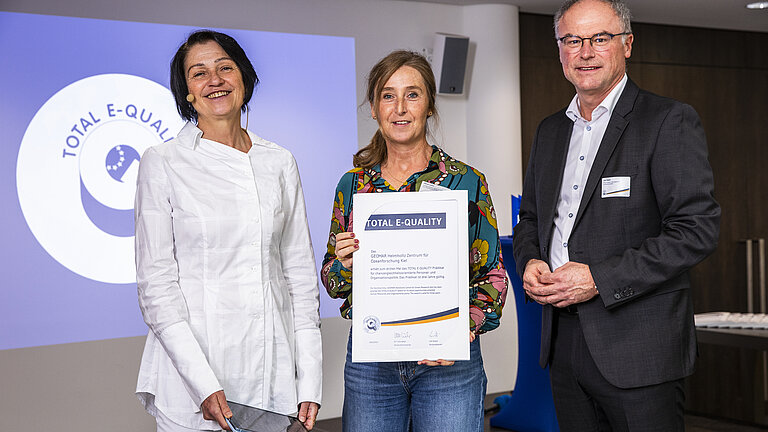 Zwei Frauen und ein Mann mit einer Urkunde