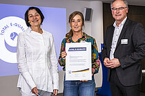 Zwei Frauen und ein Mann mit einer Urkunde