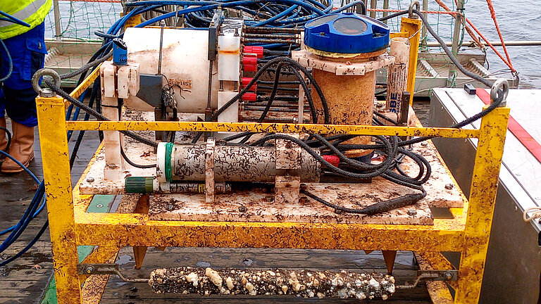 Ein schmutziges, verrostetes, mit Muscheln bewachsenes gelbes Metallgestell auf einem Forschungsschiff